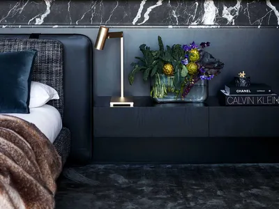 A minimalist bedroom featuring a marble headboard and a floating nightstand with a lamp and flowers.