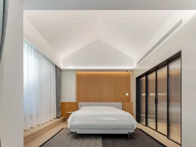 Modern minimalist bedroom with wood flooring, a bed with a minimalist grey headboard, and a rug with a clear geometric patter