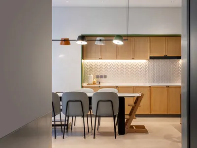 A modern, minimalist residential kitchen featuring commercial-grade lighting, wooden cabinets, and a white tile backsplash.