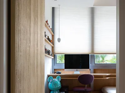 A modern home office with a wooden bench, computer setup, and shelves filled with collectibles.