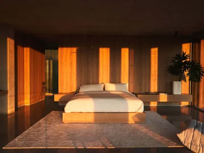 A minimalist bedroom featuring a bed on a wooden platform, surrounded by wooden walls and floor, with sunlight filtering thro