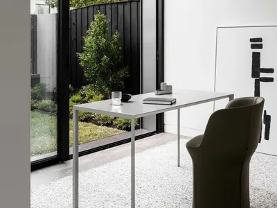 A minimalist home office featuring a metallic desk and wooden chair.