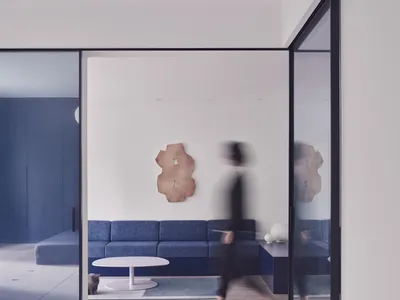 A minimalist living room with a blue fabric couch, modern coffee table, and abstract art on the wall.