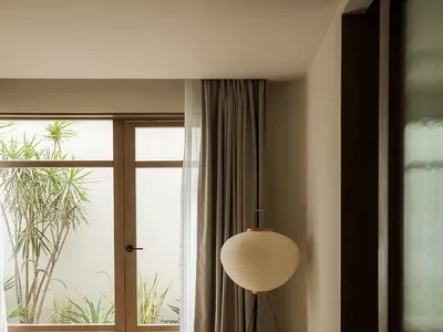 A minimalist bedroom featuring fabric curtains on a wooden floor, with a large window providing natural light.
