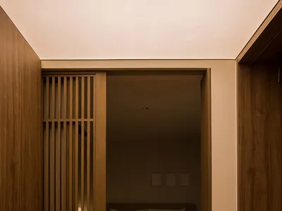 A modern minimalist bedroom with wooden walls and floor, featuring a bed with white bedding and wooden slatted headboard.