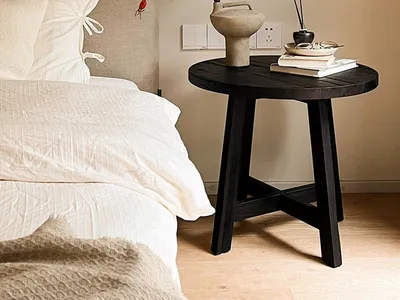 Minimalist bedroom featuring a black side table with a concrete vase, books, and incense sticks, alongside a white bed with s