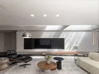 Modern minimalist living room featuring concrete walls, a white rug, and concrete furniture.
