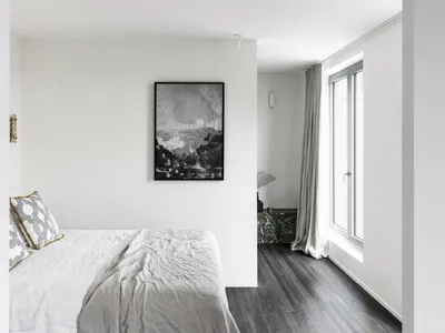 A minimalist bedroom with a white bed, gray walls, and a large window.