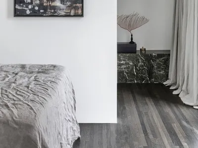 A modern minimalist bedroom featuring a bed with silver bedding and a marble wall.