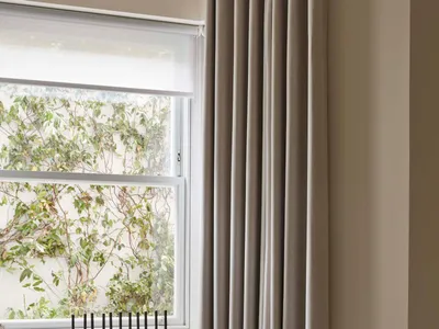 A minimalist bedroom featuring grey curtains and a modern metal sculpture by the window.