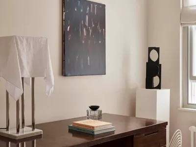 Modern minimalist home office with a wooden desk featuring abstract art and a sleek, white chair.