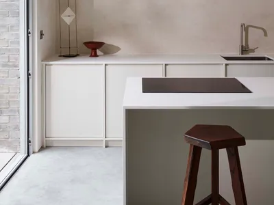 Modern, minimalist residential kitchen with white marble countertops and cabinets, featuring a central island and a sleek, co
