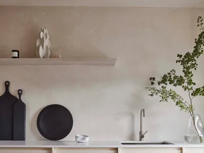 A modern minimalist kitchen features sleek white cabinets, a submerged sink, and a floating shelf with decorative items.