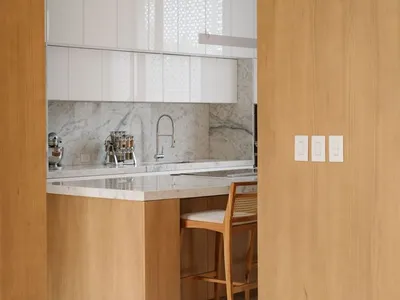 Modern kitchen featuring white marble countertops and backsplash with wooden cabinets and flooring.