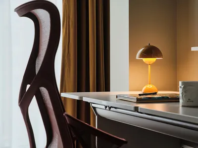 A minimalist home office with a modern desk, chair, and table lamp.