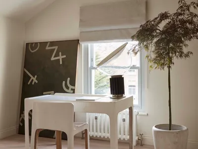 A modern home office with minimalist design, featuring a white desk, chair, and a lamp with a white shade.