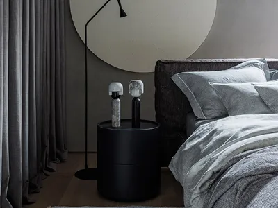 Modern minimalist bedroom with a gray fabric headboard, light gray bedding, and a textured gray rug. The room features soft,