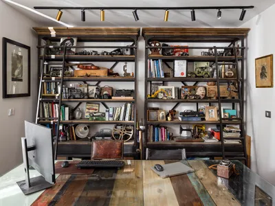 A home office with wooden shelves filled with books, cameras, and vintage items.