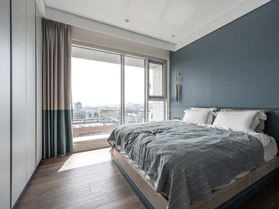 A cozy modern bedroom with a bed, fabric window curtains, and a view of the city.