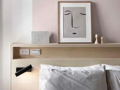 A minimalist bedroom with a wooden headboard and a framed abstract face drawing on the wall.
