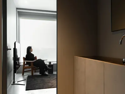 A minimalist home office setup with a wood chair and table, framed by a large window.