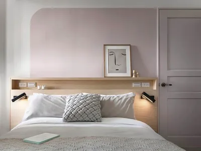 A modern minimalist bedroom with a wooden headboard, white bedding, and a grey woven pillow.