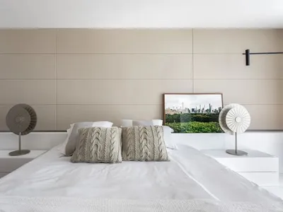 A modern, minimalist bedroom with a white bed, beige wall paneling, and decorative pillows.