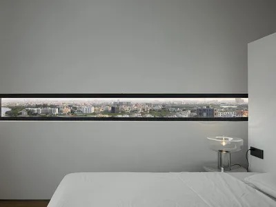 Modern minimalist bedroom featuring white walls and a city view through a horizontal window.