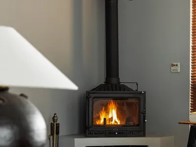 A modern industrial-style living room featuring a freestanding stove with a high chimney and a wood storage area below, surro