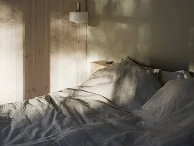 A minimalist bedroom with wooden walls and fabric bedding, featuring natural light and a hanging lamp.
