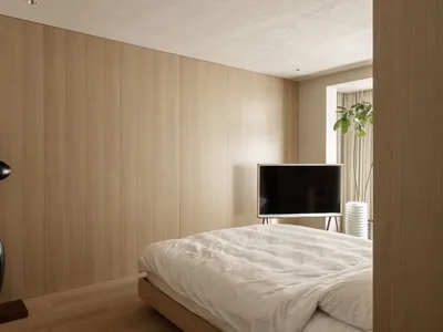A minimalist bedroom with white wooden walls and a black abstract sculpture, featuring a bed with white sheets and a televisi