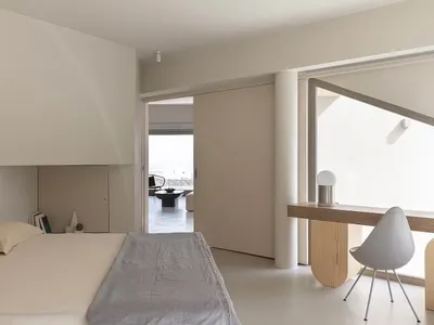 A minimalist bedroom with white furniture and a grey bedspread.