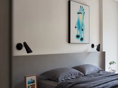 A minimalist bedroom with a grey fabric bed and white side table.