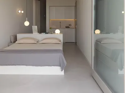 Modern minimalist bedroom with concrete walls and floor, featuring a single bed and a small kitchenette.