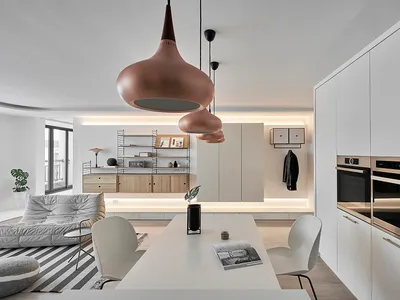 A modern, minimalist kitchen and dining area featuring white cabinets and a white table with a geometric pendant light fixtur