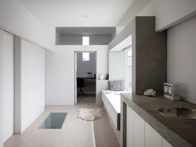 A minimalist kitchen with concrete walls and floor, featuring a white sink and a window.