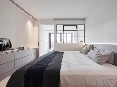 Modern minimalist bedroom with white furniture and black accents, featuring a large bed with a grey upholstered headboard and