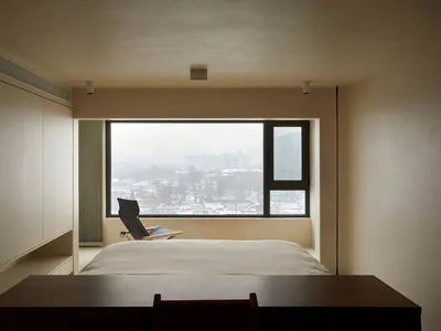 簡約臥室內設有大型窗戶，窗外可見雪景城市景觀，房間內擺放床鋪、椅子與書桌。