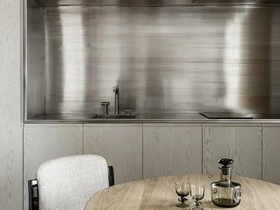 A minimalist modern kitchen with metallic finishes and a round wooden table.