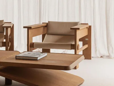 A minimalist living room featuring a wooden couch and table, with sheer white curtains in the background.
