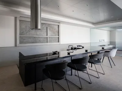 Contemporary kitchen with minimalist design, featuring black countertops and neutral-colored chairs.