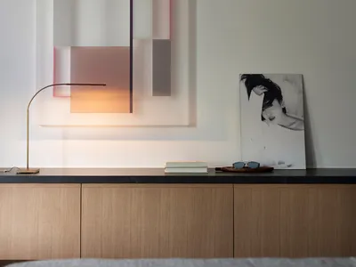 A minimalist bedroom featuring a colorful geometric wall artwork and wooden cabinets.
