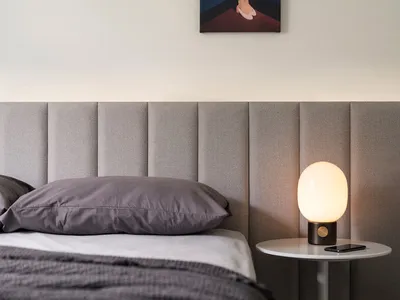 A minimalist bedroom featuring a bed with a upholstered fabric headboard and matching bedding, accompanied by a round side ta