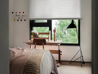 A minimalist bedroom with wooden furniture, a bed, a desk, and a window with greenery outside.