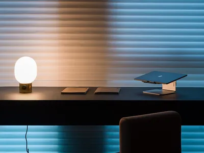 A minimalist home office setup featuring a sleek, metallic desk with a modern, glass lamp and a functional, stylish notebook.