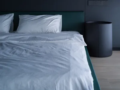 Minimalist bedroom with a white bed, green headboard, and a black bedside table with a lamp.