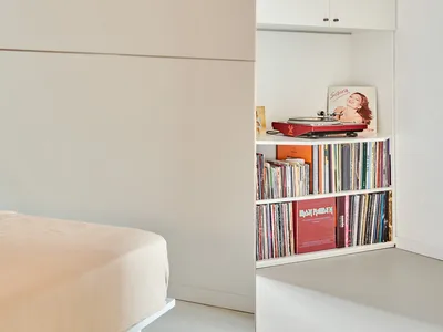 A minimalist bedroom featuring white cabinets with vinyl records and a turntable.