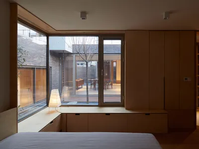A minimalist bedroom with wooden cabinets and a large window overlooking a courtyard.