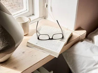 A minimalist bedroom featuring a wooden table with a book, glasses, and a mug.