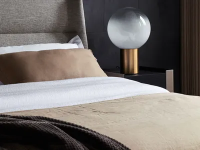 A modern minimalist bedroom with fabric bedding and a glass and metal lamp on a nightstand.